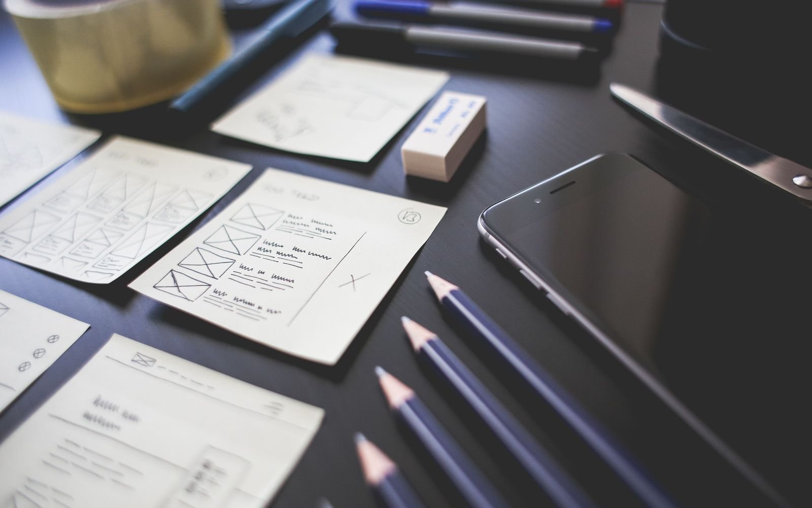 Hand drawn website wireframe sketches next to a smartphone and pencils on a desk